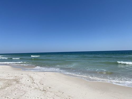 A serene beach scene with gentle waves, soft sand, and a clear blue sky.