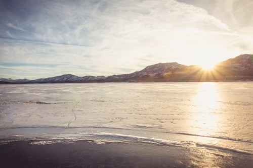 Sunset over a frozen lake, with mountains in the background and a clear sky reflecting warm light.