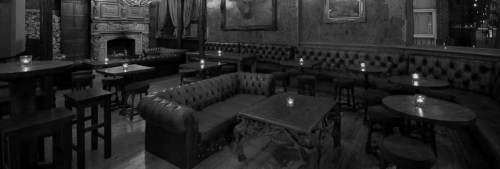 A dimly lit lounge with leather seating, wooden tables, and candles creating a cozy atmosphere.