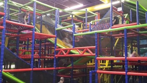Colorful indoor play structure with multiple levels, slides, and children playing throughout the maze-like setup.