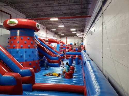 A colorful indoor inflatable playground with slides and obstacles, filled with children playing and having fun.