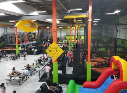 A vibrant indoor trampoline park filled with people jumping, playing, and relaxing in a colorful, energetic environment.
