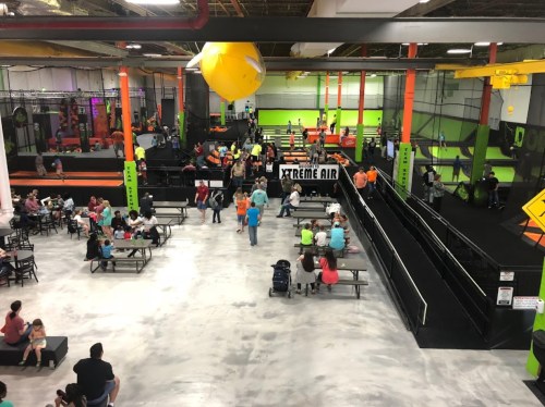 A vibrant indoor trampoline park with people enjoying activities, colorful decor, and seating areas.