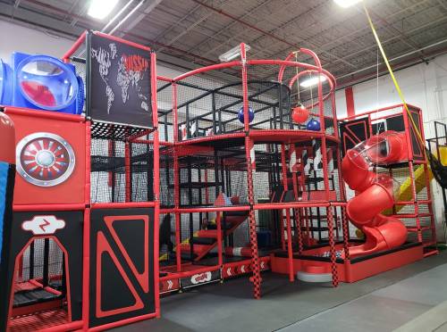 Colorful indoor playground with slides, climbing structures, and various play areas in red and black.