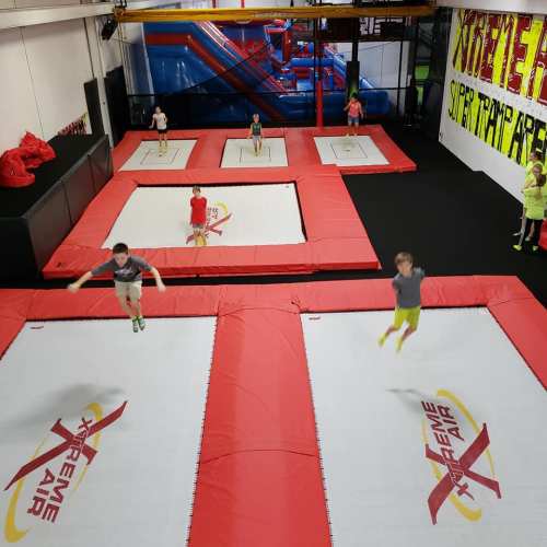 Kids jumping on large red trampolines in a vibrant indoor trampoline park.