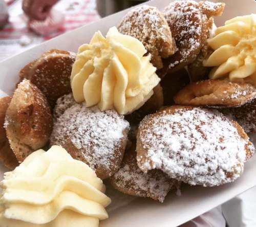 A plate of small, round pastries dusted with powdered sugar and topped with swirls of cream.