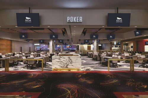A spacious poker room with multiple tables, screens displaying the MGM logo, and modern decor.