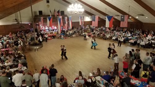 A lively dance event in a large hall, with couples dancing and flags displayed around the room, filled with spectators.