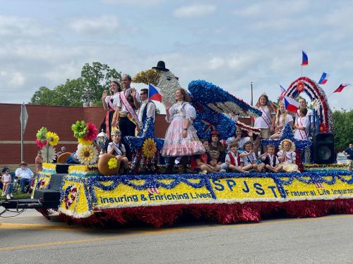 A colorful parade float decorated with flowers, featuring people in traditional attire celebrating a festive event.