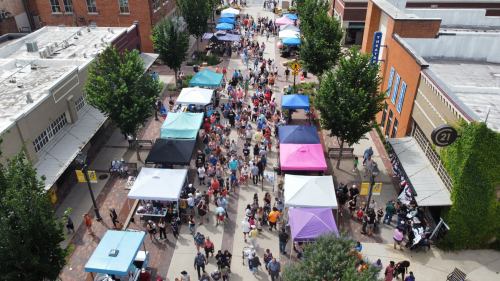 Aerial view of a bustling street market with colorful tents and a large crowd of people enjoying the event.