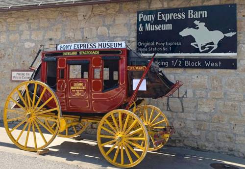 A vintage stagecoach outside the Pony Express Barn & Museum, with a sign featuring a horse and rider.