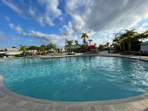 A clear blue pool surrounded by palm trees and lounge chairs under a partly cloudy sky.