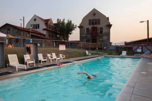 A swimming pool with a swimmer in action, surrounded by empty lounge chairs and old buildings in the background.
