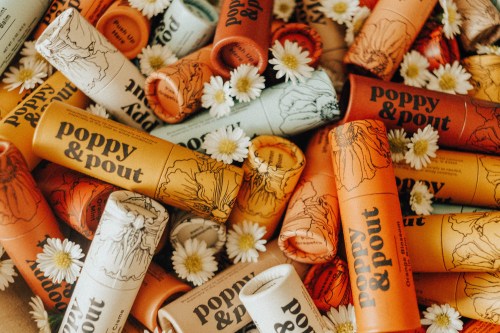 A colorful assortment of Poppy & Pout lip balms surrounded by small white daisies.