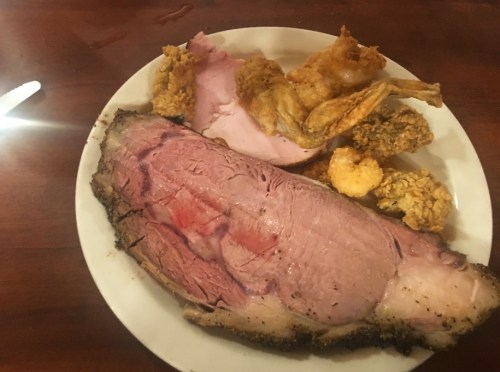 A plate with slices of roast beef, fried chicken, and shrimp, served on a wooden table.