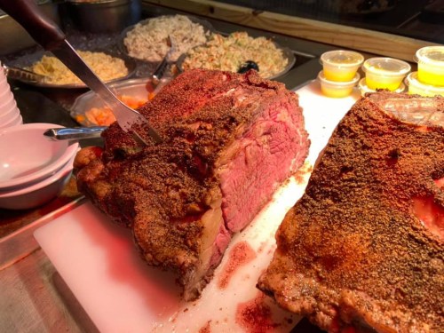 A close-up of a seasoned roast beef being sliced, with side dishes and sauces in the background.