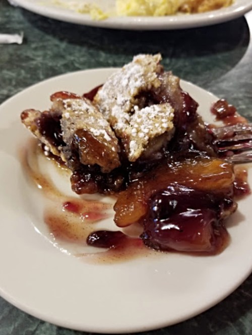 A plate of dessert featuring fried dough pieces topped with powdered sugar and a berry sauce.