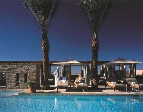 A serene poolside scene with palm trees, lounge chairs, and a person relaxing under a canopy at dusk.