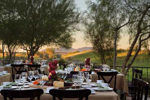 Elegant outdoor dining setup with tables adorned with dishes and glassware, surrounded by trees and mountains in the background.