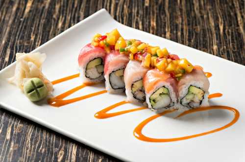 A plate of sushi rolls topped with mango salsa, accompanied by wasabi and pickled ginger on a wooden table.