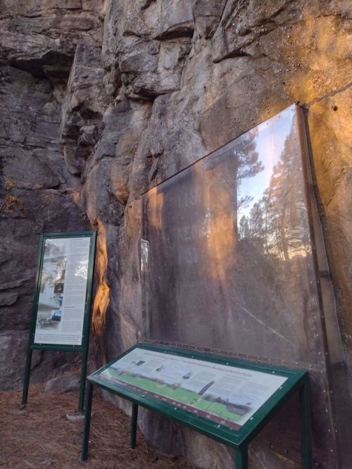 Information panels are displayed against a rocky cliff, surrounded by trees and soft evening light.