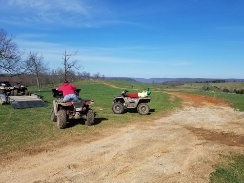Two ATVs parked on a dirt path in a scenic landscape with rolling hills and clear blue skies.