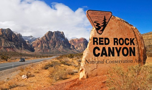 Sign for Red Rock Canyon National Conservation Area with mountains and a blue sky in the background.