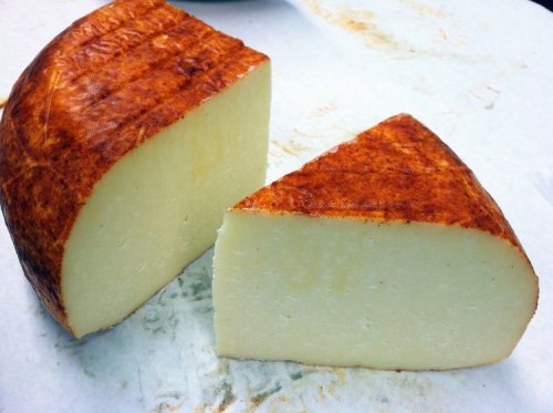 A round wheel of cheese with a reddish-brown rind, partially sliced to reveal a creamy white interior.