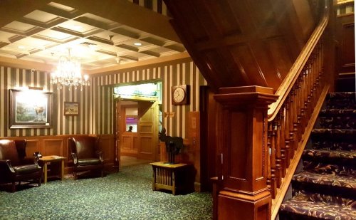 A cozy lobby with wooden accents, a staircase, and plush seating, featuring striped walls and a chandelier.