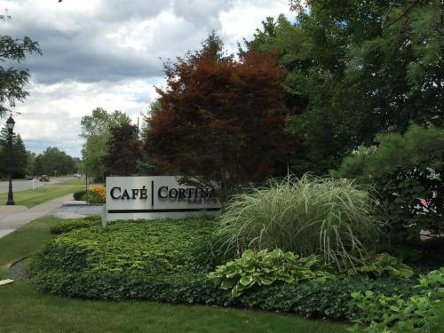 Sign for Café Cortina surrounded by lush greenery and colorful plants on a cloudy day.