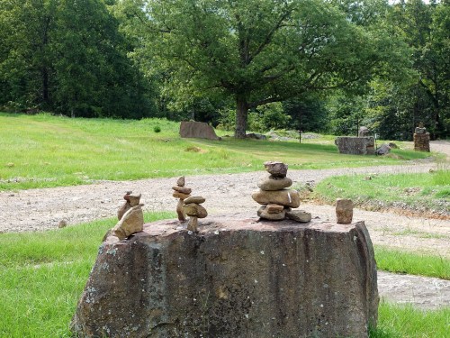 A rock formation with stacked stones on a large boulder, surrounded by green grass and trees in a natural setting.