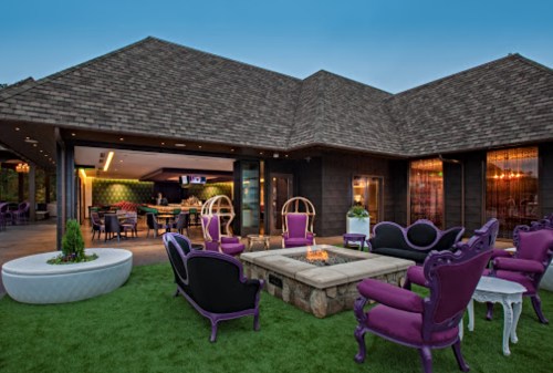 A stylish outdoor lounge area with purple chairs, a fire pit, and a modern home in the background.