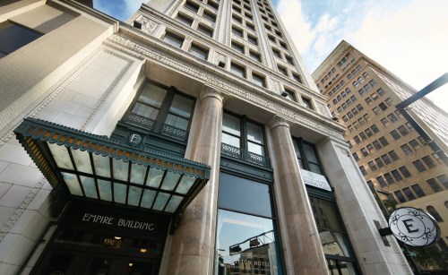 View of the Empire Building's entrance, showcasing its architectural details and tall structure against a blue sky.
