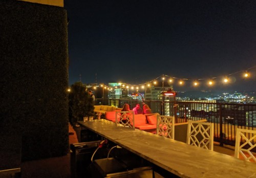 Rooftop lounge at night with string lights, colorful seating, and a city skyline in the background.