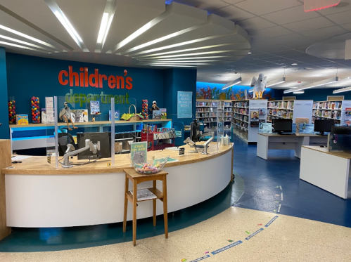 Bright children's library with colorful decor, bookshelves, and a welcoming service desk.