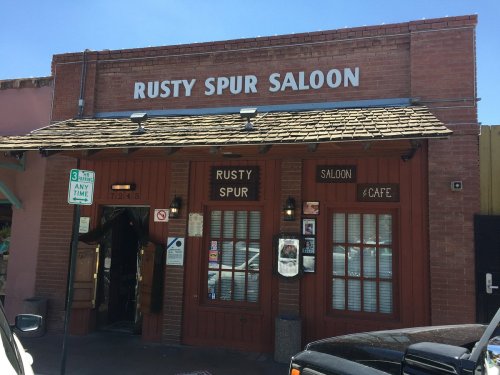 Exterior of the Rusty Spur Saloon, a brick building with a sign, doors, and a clear blue sky above.
