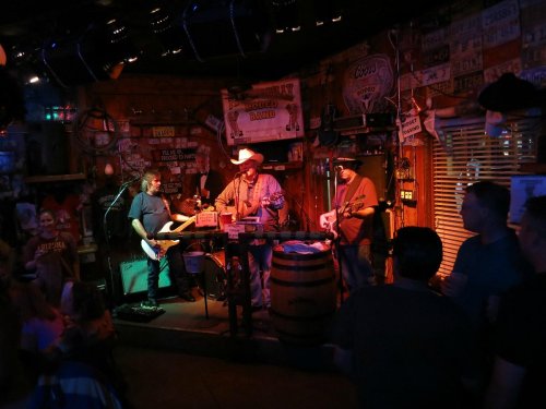 A lively band performs on stage in a rustic venue, with an engaged audience enjoying the music.