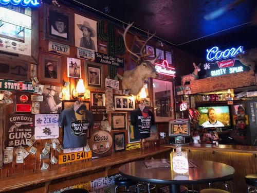 A rustic bar interior featuring vintage photos, memorabilia, a mounted deer head, and a TV in a cozy atmosphere.