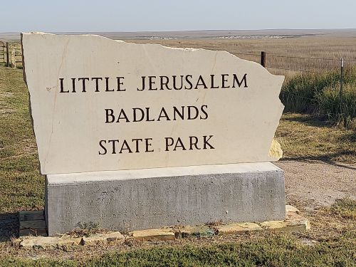 Sign for Little Jerusalem Badlands State Park, featuring large stone letters against a grassy landscape.
