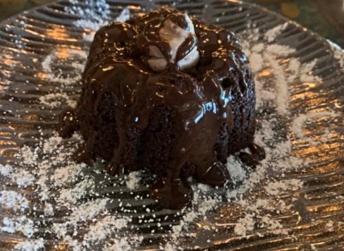 A rich chocolate dessert topped with melted chocolate and a dollop of cream, served on a decorative plate.