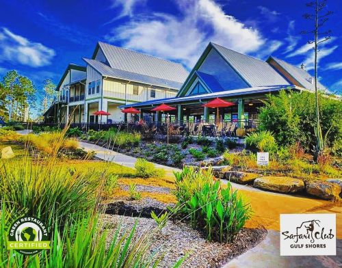 A scenic view of a restaurant with outdoor seating, surrounded by greenery and a clear blue sky.