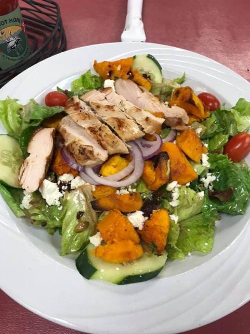 A colorful salad with grilled chicken, roasted squash, cucumbers, cherry tomatoes, and mixed greens on a white plate.