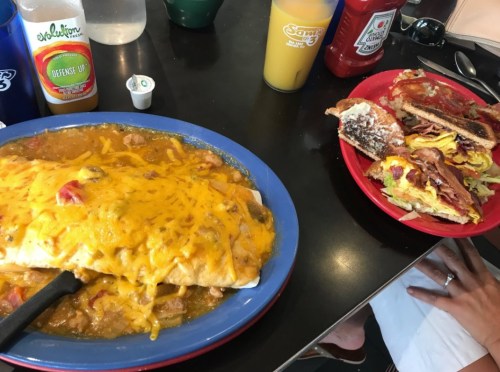 A plate with a large smothered burrito topped with cheese, next to a plate of a sandwich filled with bacon and eggs.