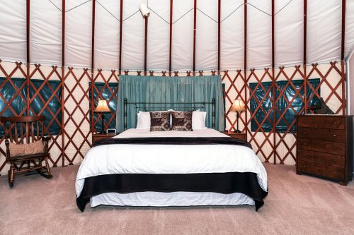 Cozy yurt interior featuring a bed, wooden dresser, rocking chair, and soft lighting.