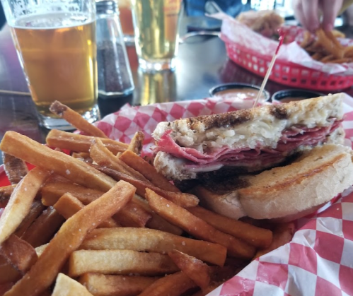 A plate with a sandwich filled with meat and cheese, served with a side of crispy fries and a drink in the background.