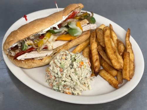 A large sandwich with turkey, peppers, and condiments, served with fries and a side of pasta salad on a white plate.