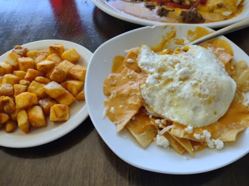 A plate of nachos topped with cheese, an egg, and a side of golden-brown potato cubes.