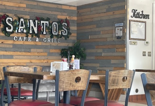 Interior of Santos Cafe & Grill featuring wooden walls, tables, and a sign for the kitchen. Cozy dining atmosphere.