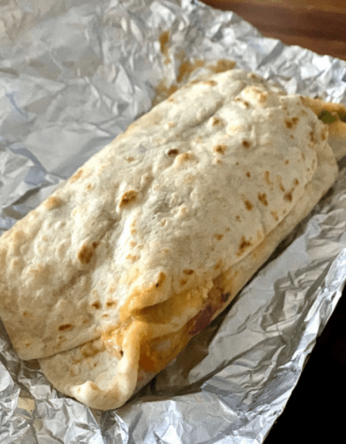 A wrapped burrito in foil, featuring a soft tortilla filled with cheese and vegetables.