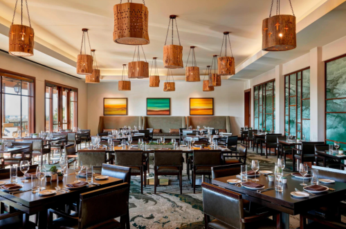 Elegant restaurant interior with wooden pendant lights, dark furniture, and artwork on the walls, set for dining.